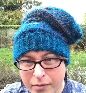Head shot of woman with glasses wearing blue fluffy crocheted hat in garden