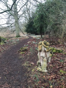Broken statue of 3 half-clad women from back, roman/greek style, with part of legs missing, by a woodland path